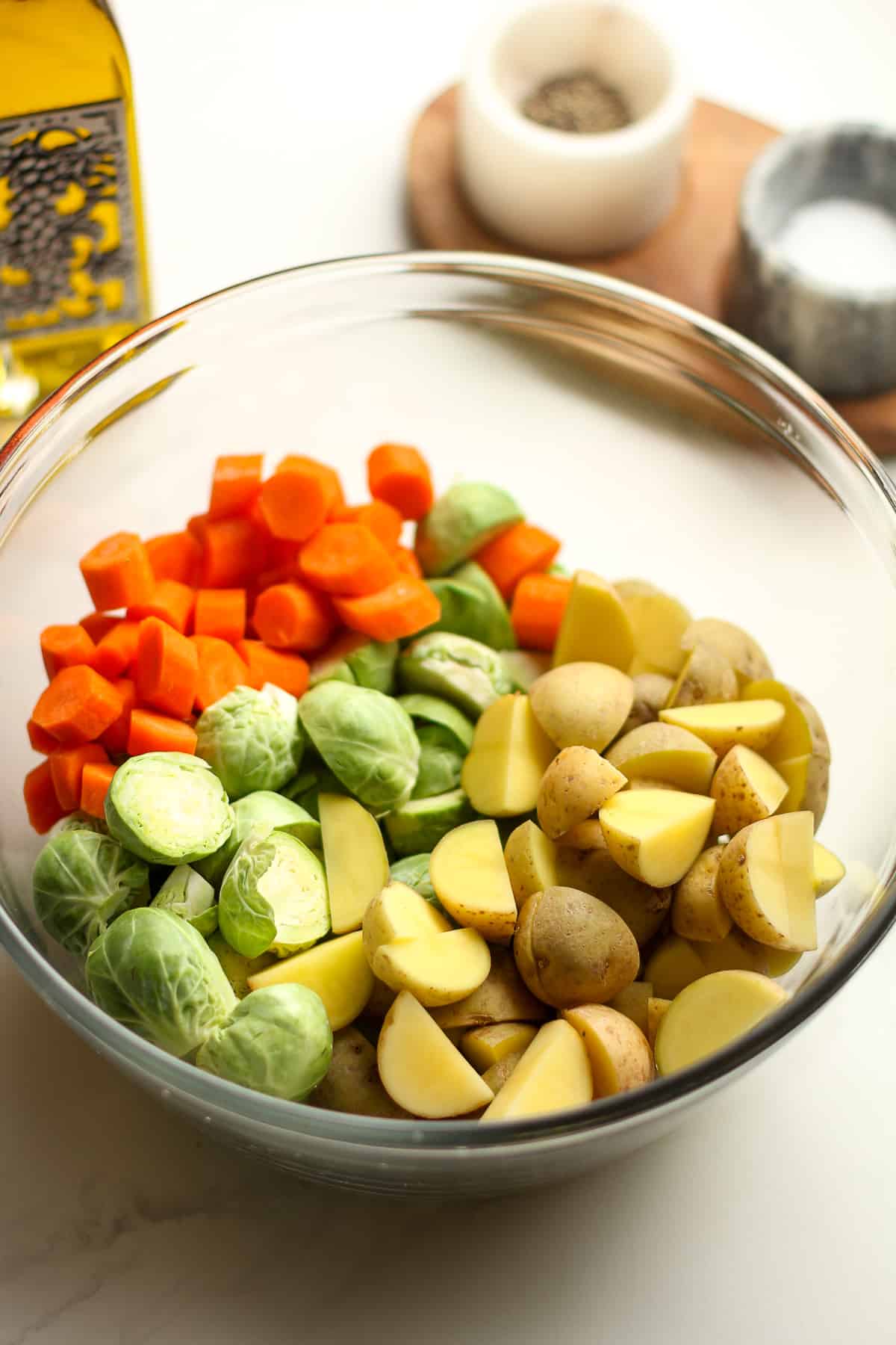 Side view of a bowl of chopped veggies, with a bottle of olive oil in the background.