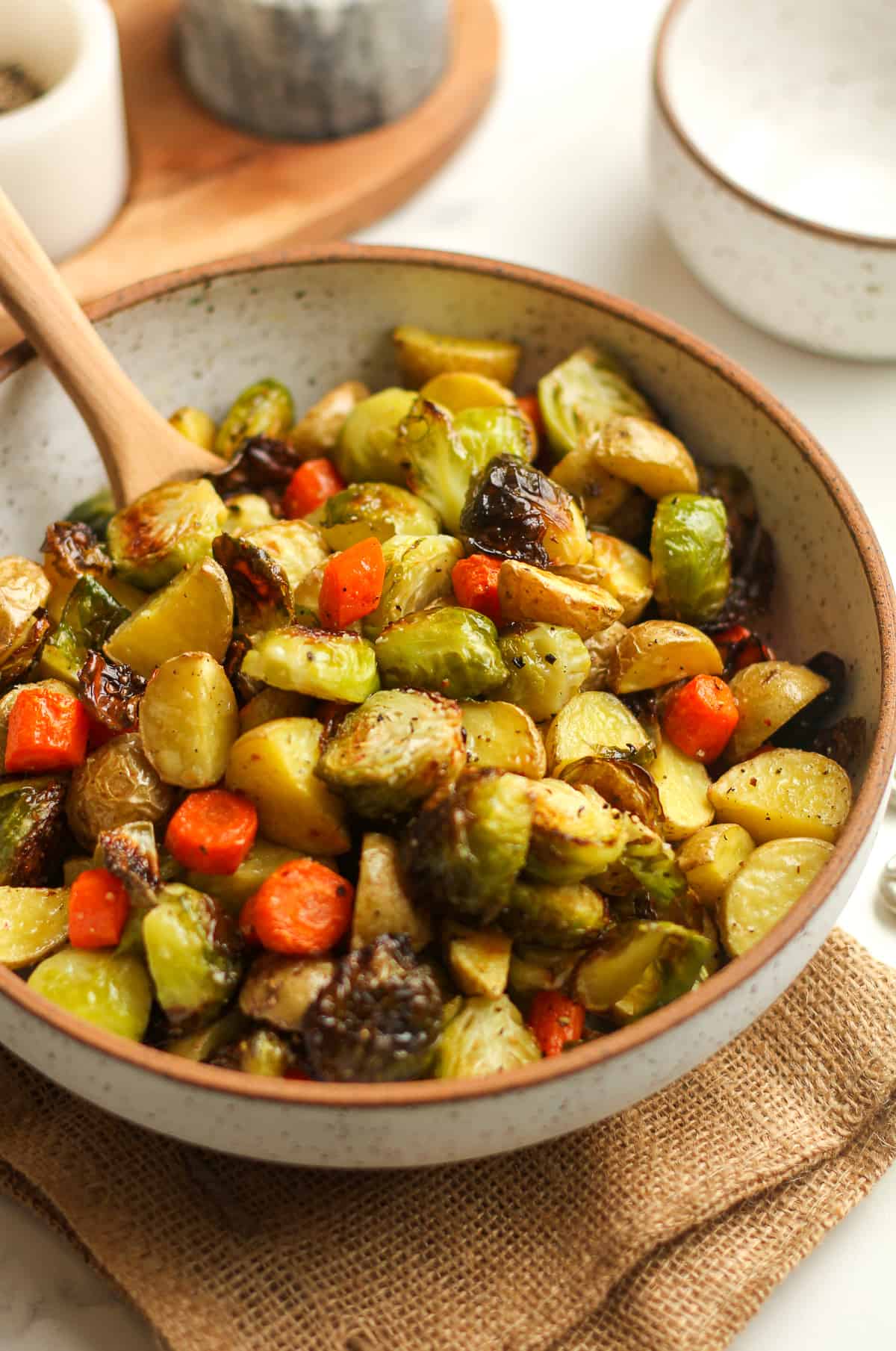 Side view of a bowl of roasted veggies, with a spoon.
