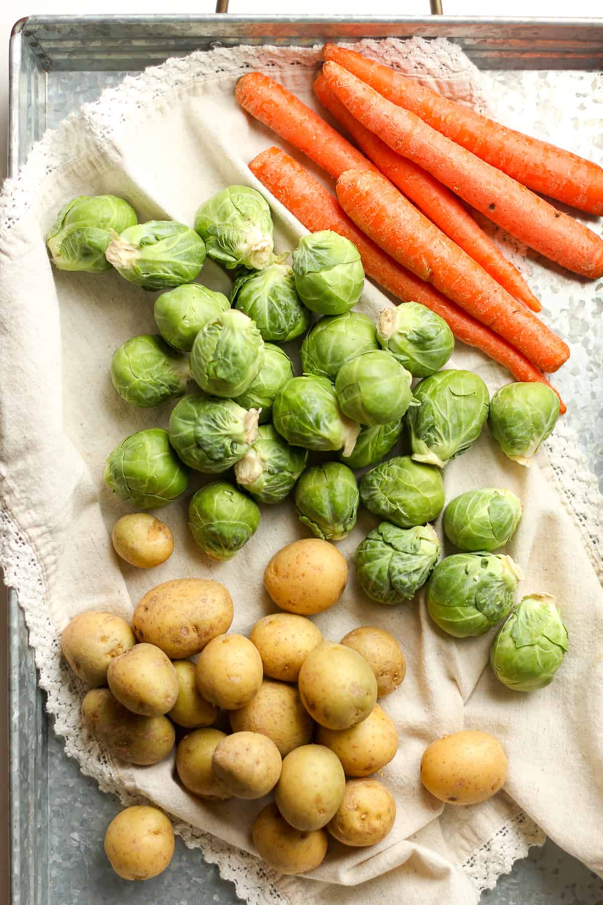 A tray of whole carrots, Brussels sprouts, and potatoes.