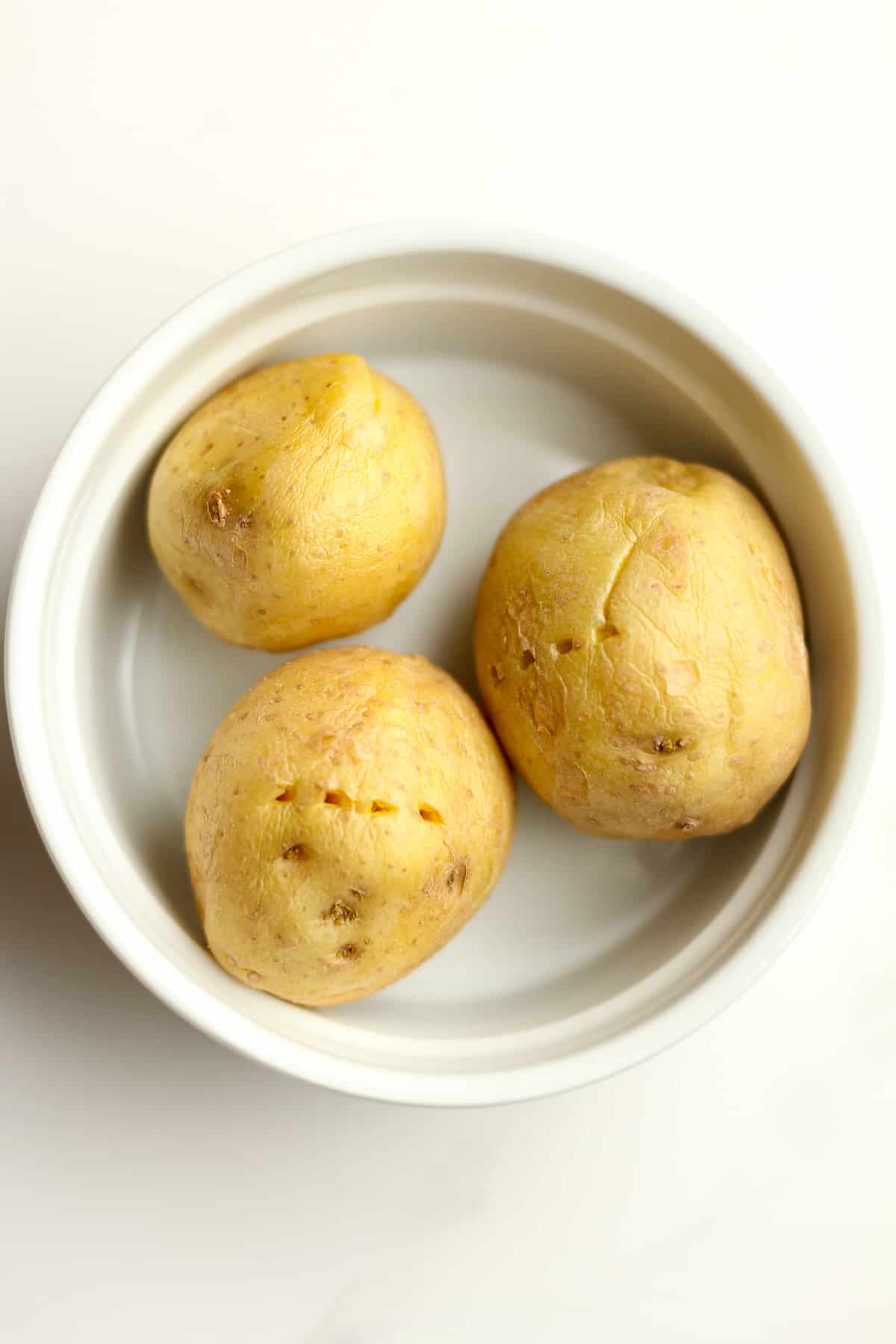 A bowl of three small yellow microwaved potatoes.