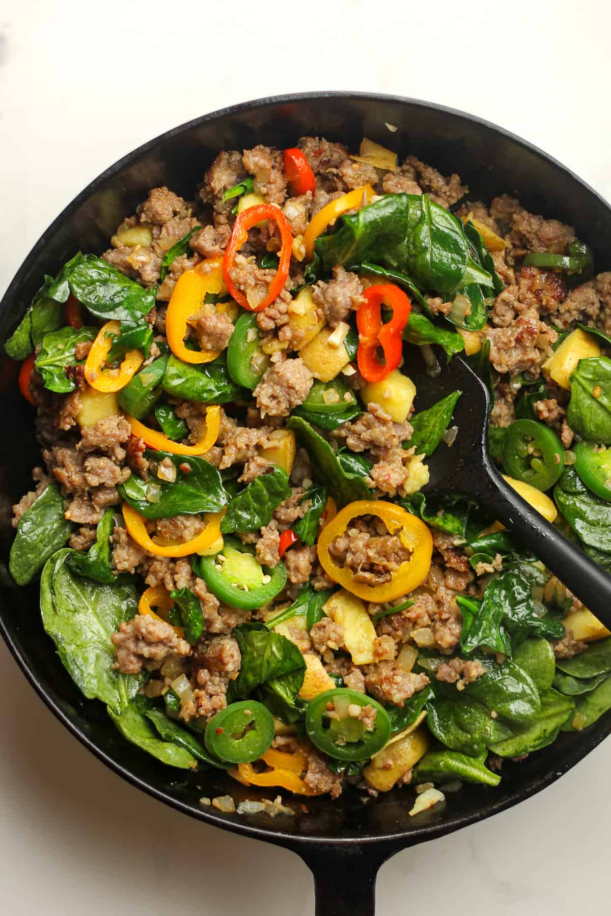 A skillet of the sausage, veggies, with spinach added in.