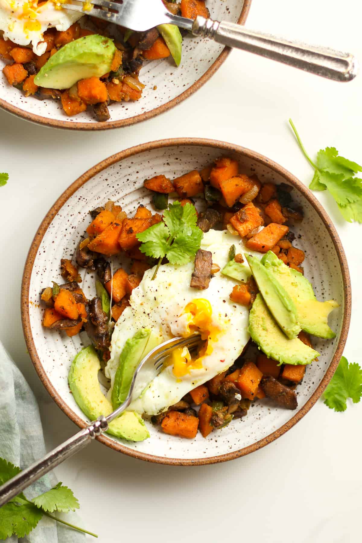 Two bowls of the sweet potato hash with broken eggs with forks.