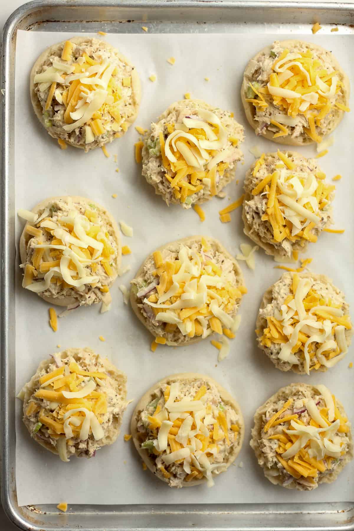 A pan of halved muffins with tuna salad and cheese on top.
