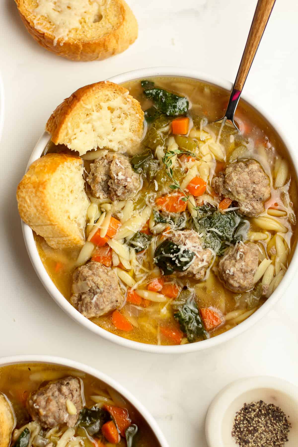A bowl of meatball soup with orzo and veggies.