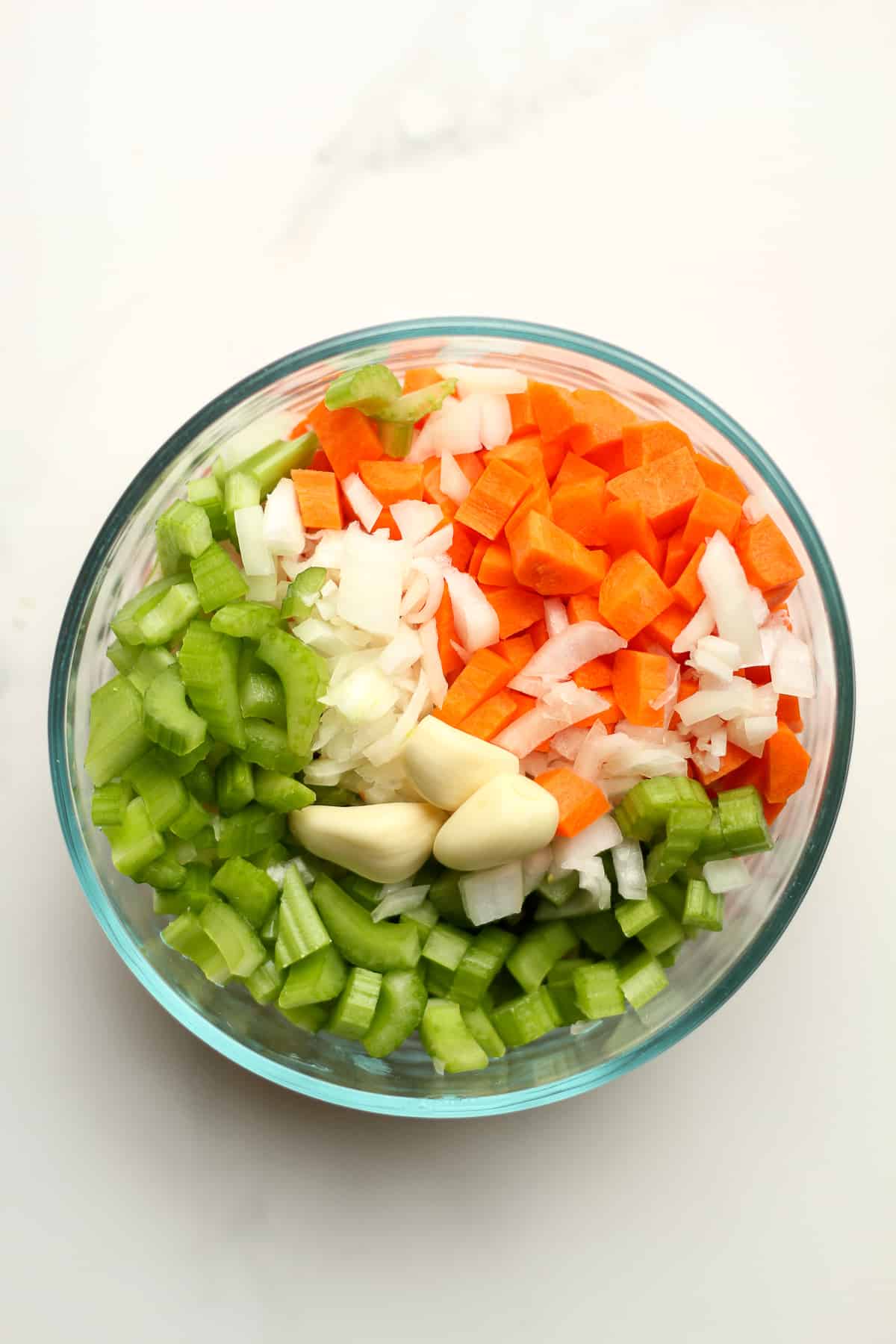 A bowl of diced carrots, celery, onion, and cloves of garlic.