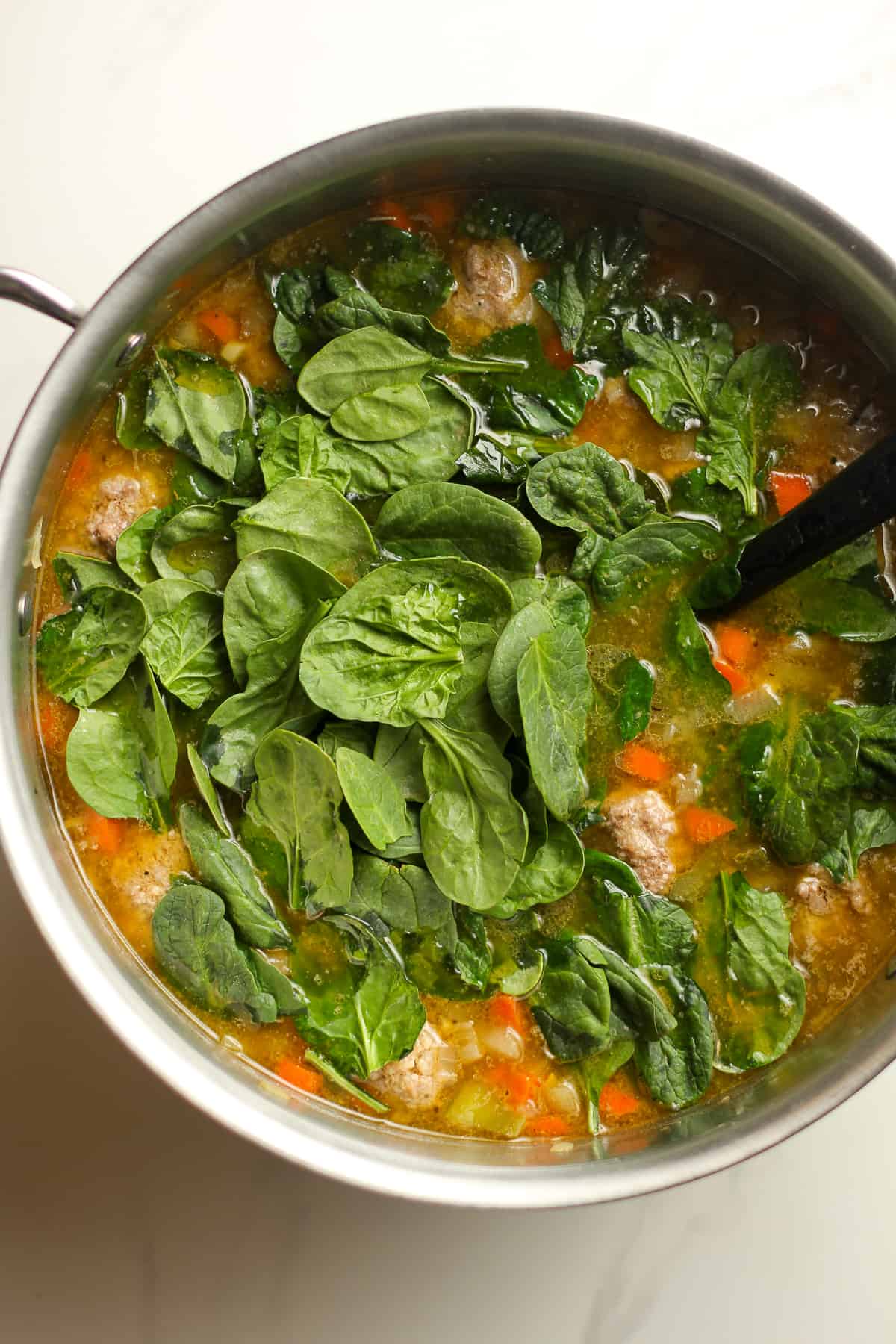A pot of the soup after the spinach is added in on top.