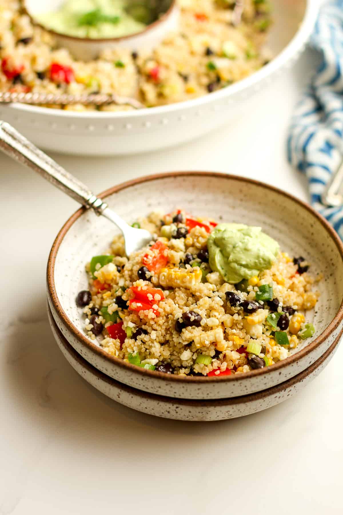 Side view of two stacked bowls with quinoa salad and a fork.