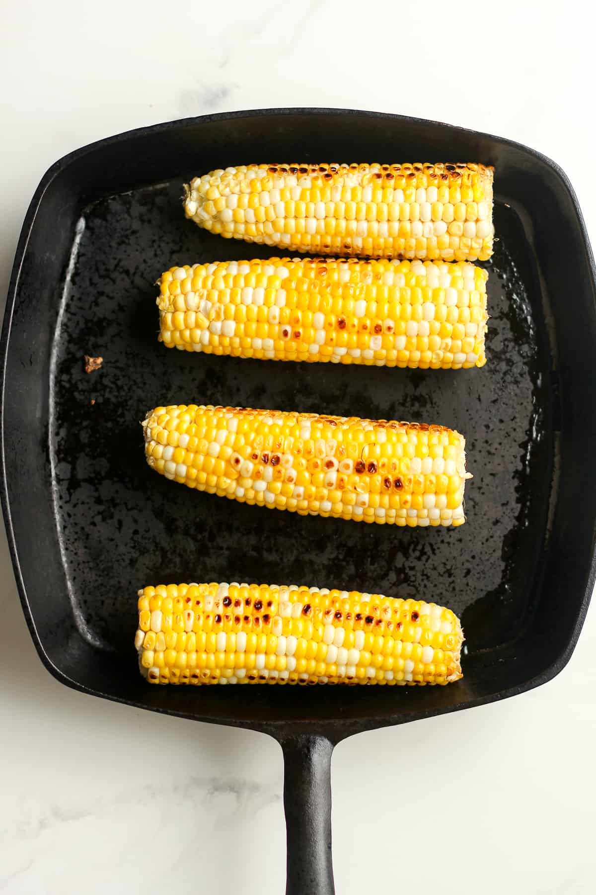 A cast iron skillet with four ears of corn.
