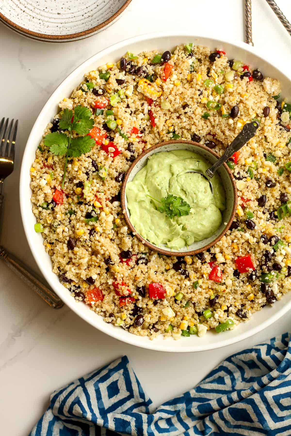 A large white salad bowl with the quinoa salad and a small bowl of avocado crema inside the bowl.