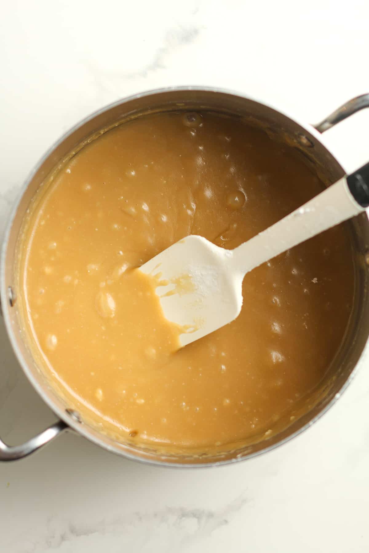 A pan of the just cooked caramel frosting with a spatula.