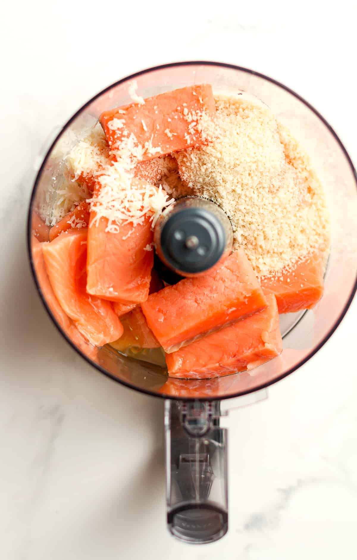 A food processor with the ingredients for salmon burgers.