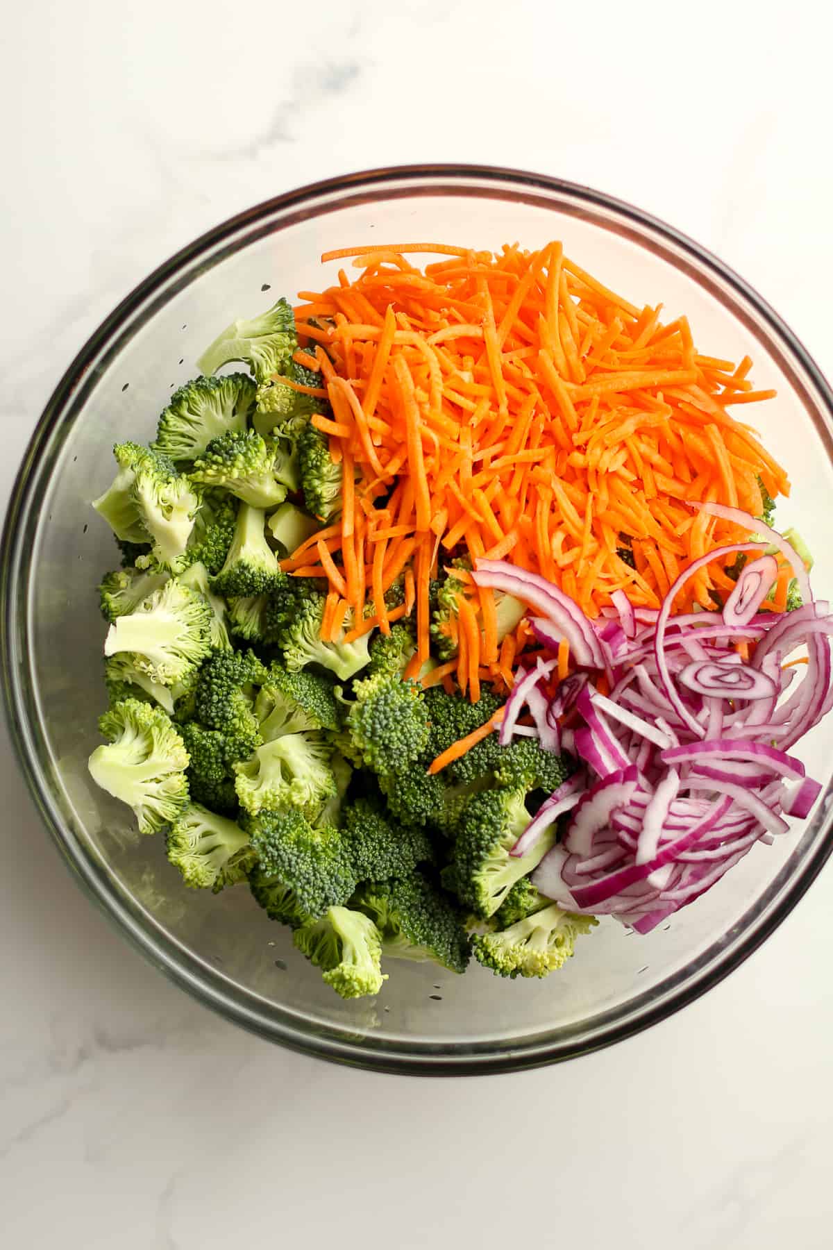 A bowl of the broccoli florets, shredded carrots, and sliced red onions.