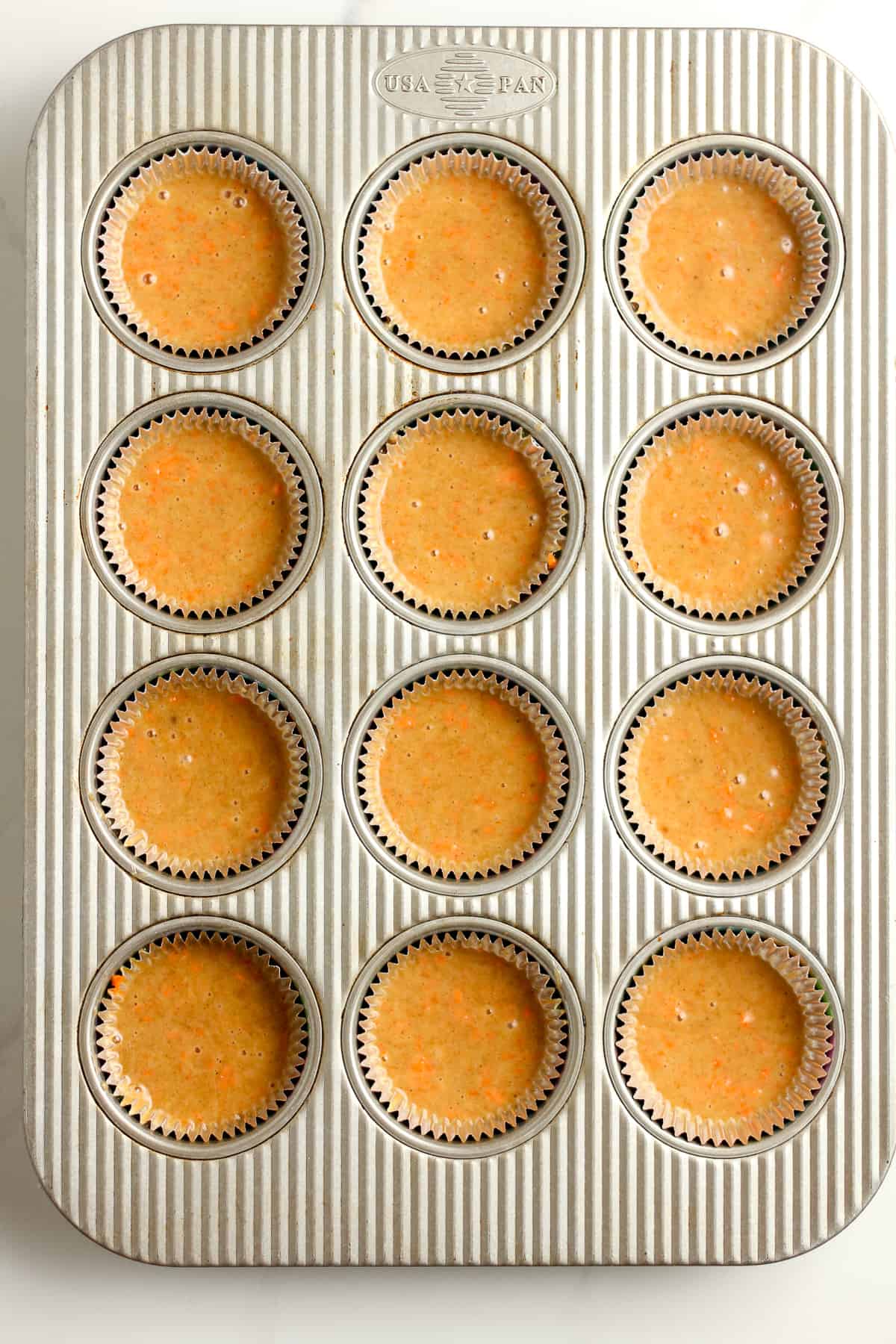 A 12-cup muffin tin filed with liners and carrot cake batter.