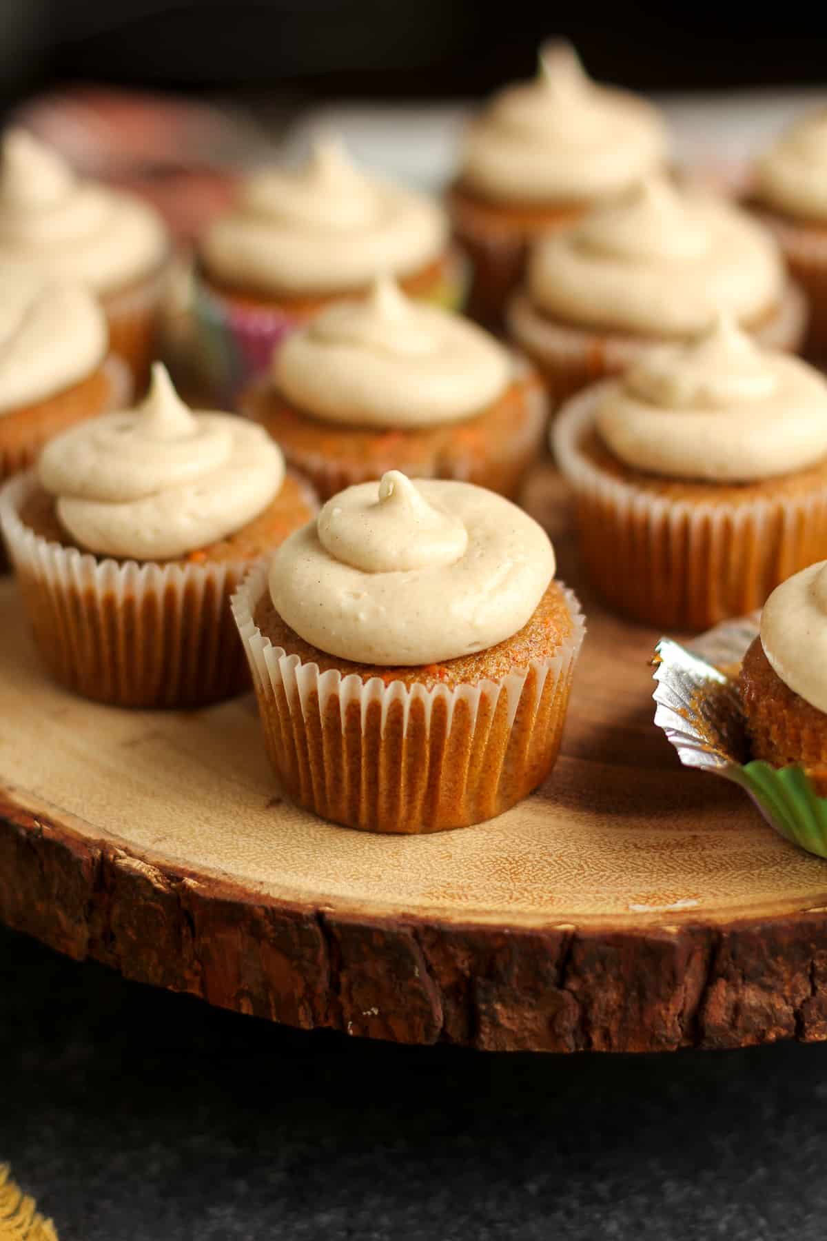 Side view of carrot cake cupcakes with cream cheese icing, all on a wooden cake stand.