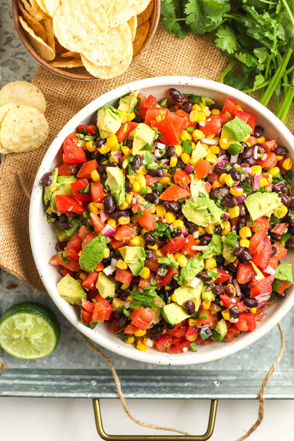 A bowl of cowboy caviar dip on a tray with some chips beside it.