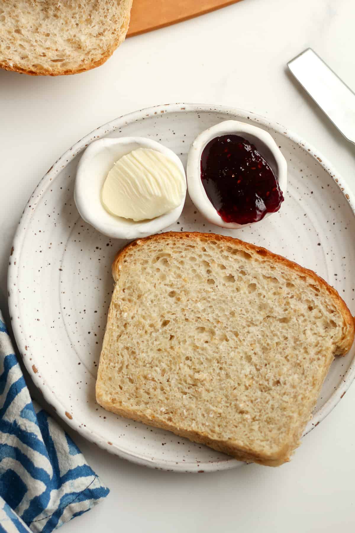 A plate with a slice of bread, with two small bowls of butter and jelly.