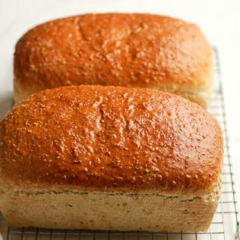 Side view of two loaves of cracked wheat bread on a cooling rack.
