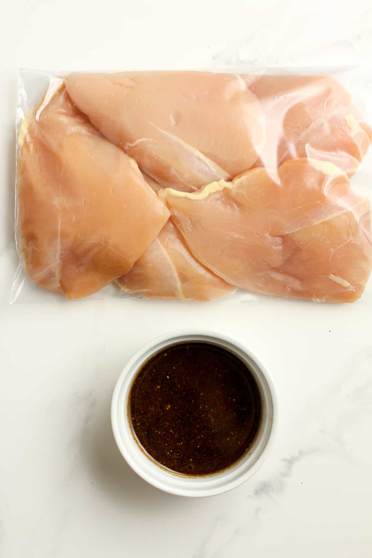 A bag of chicken breasts next to a small bowl of marinade.