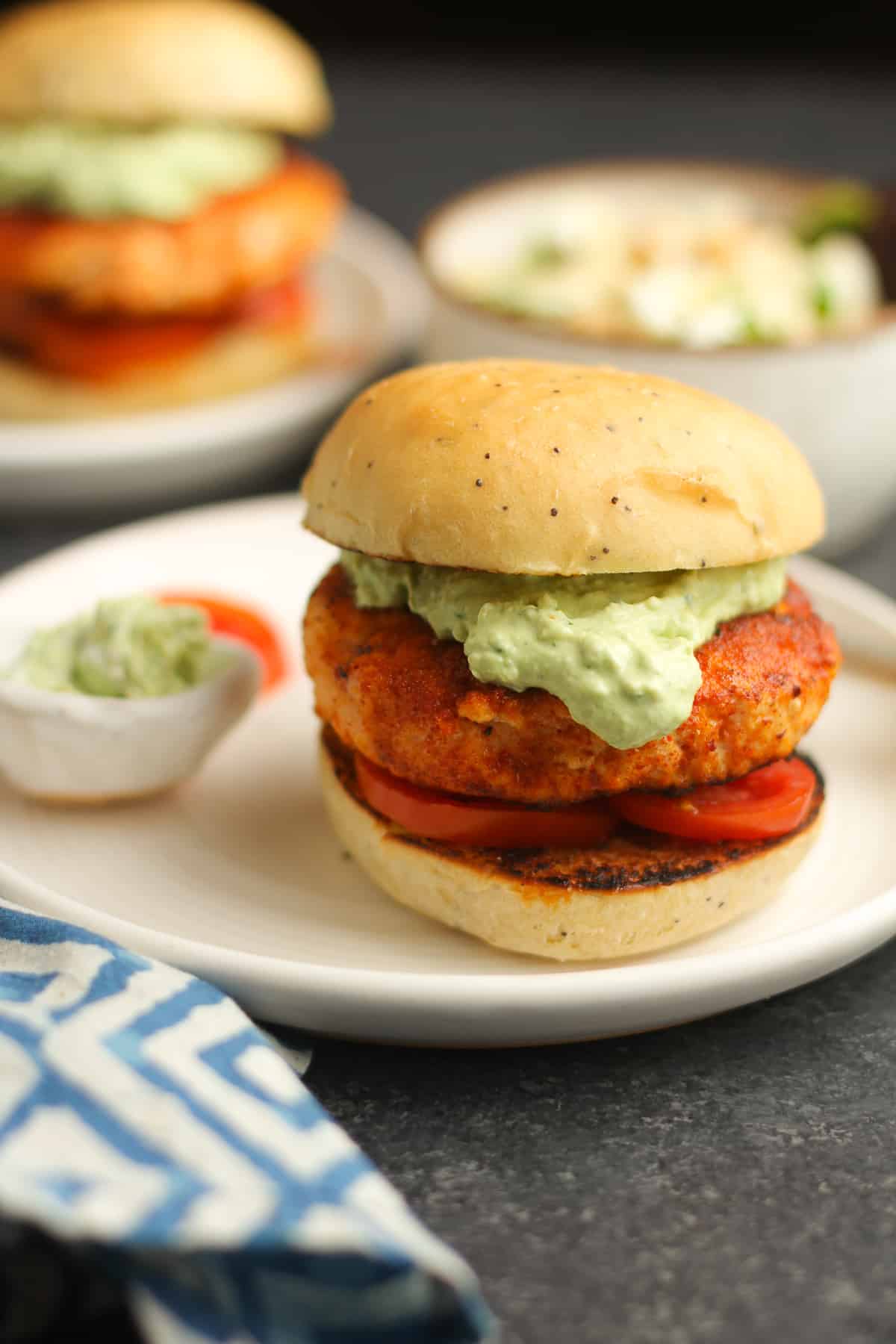 Side view of two grilled salmon burgers on homemade buns, with tomatoes and crema.