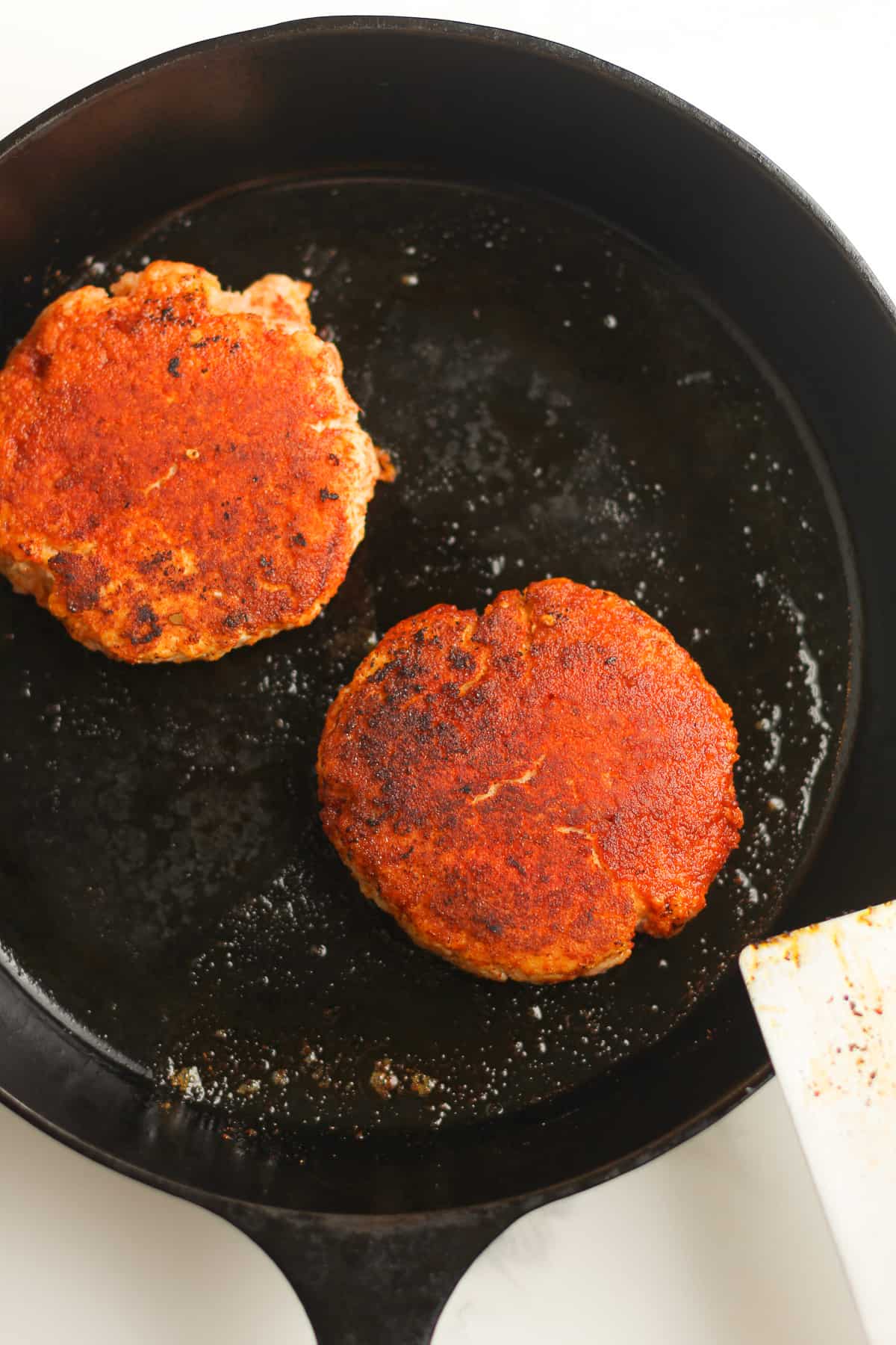 A cast iron skillet with two large salmon burgers cooking.