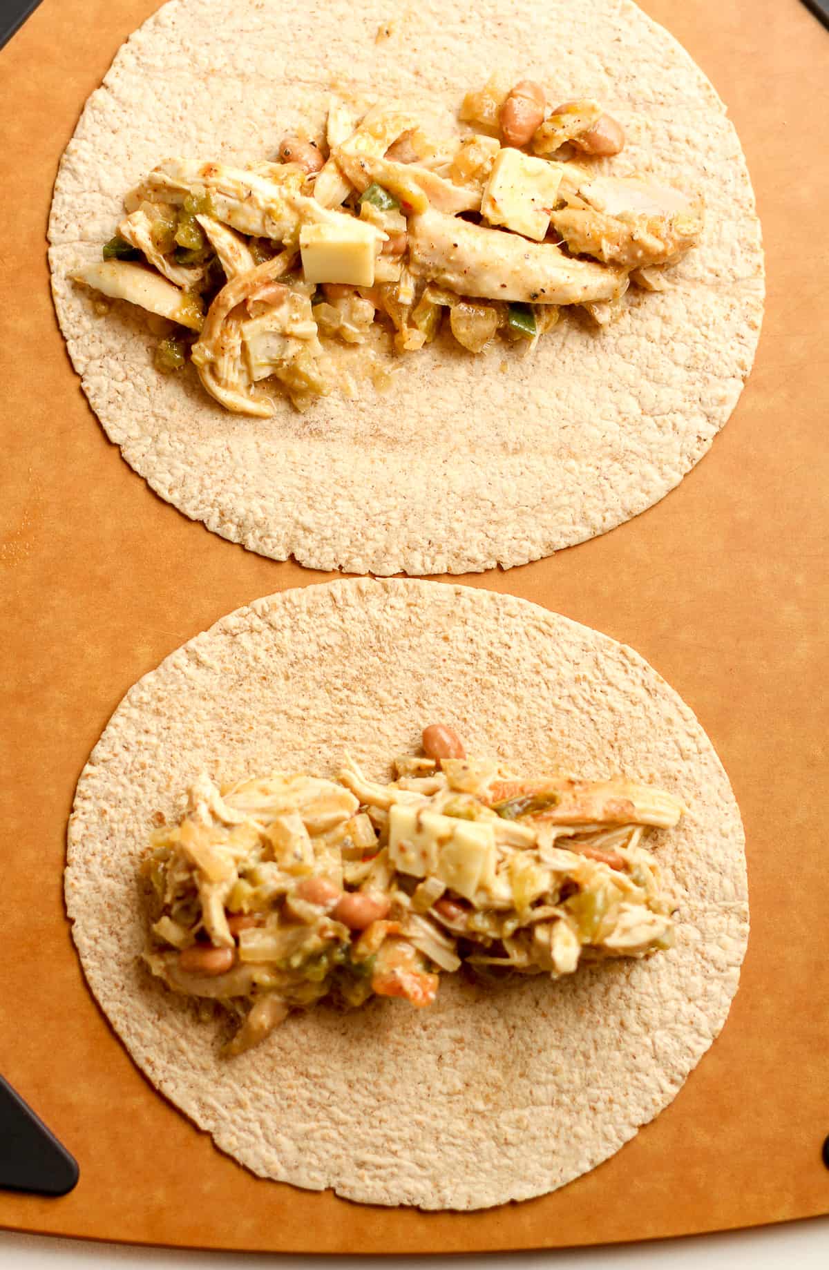 A board with two whole wheat tortillas with filling on top.
