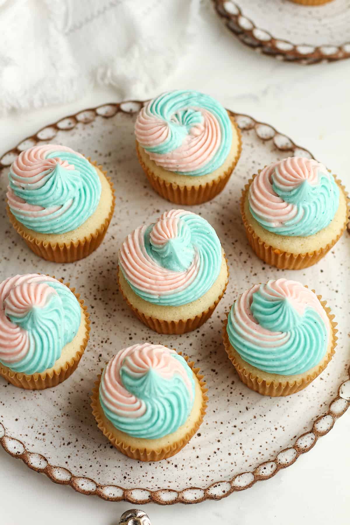 Side shot of a plate of vanilla cupcakes with swirl buttercream.