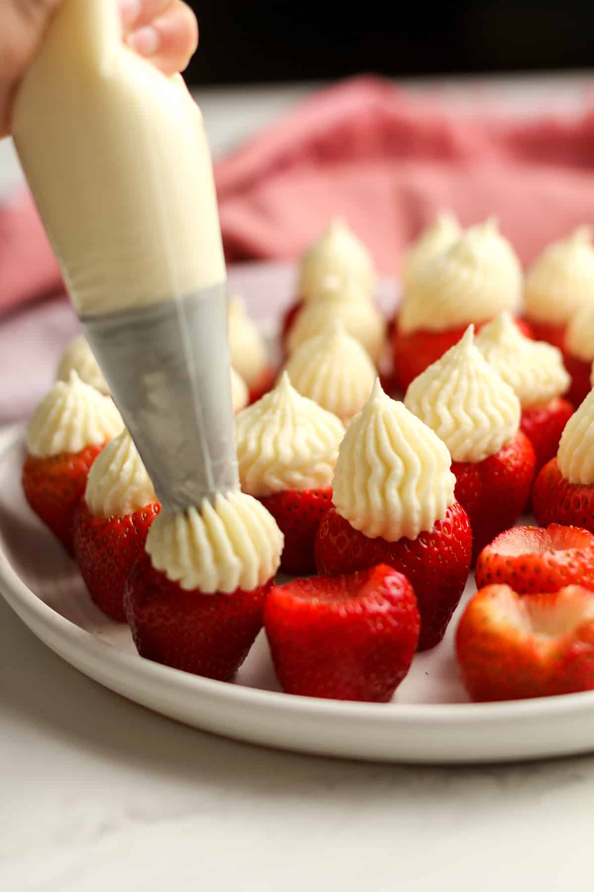 My hand squeezing the cream cheese filling on to the hulled strawberries.