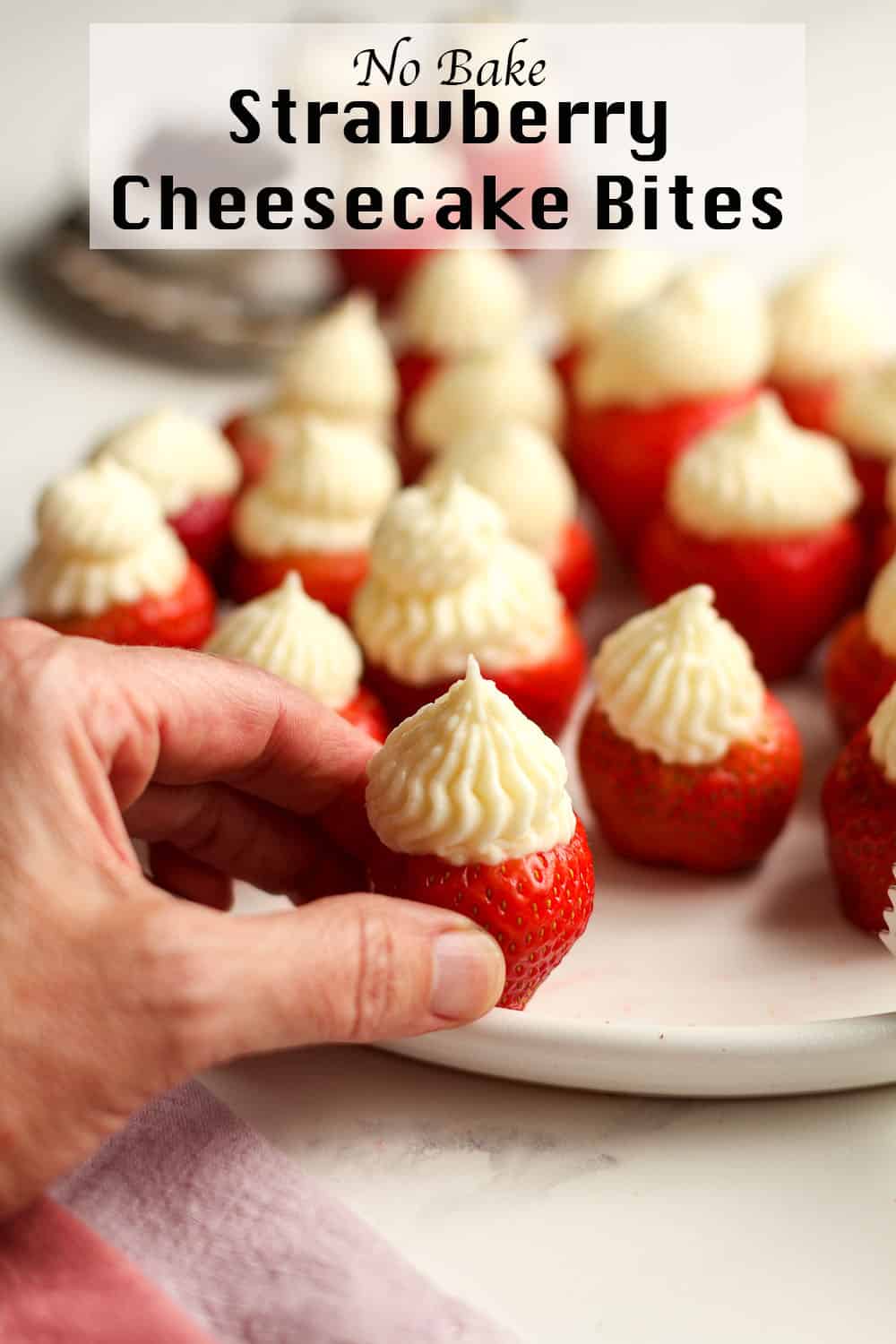 Side view of a plate of strawberry cheesecake bites, with a hand reaching for one.