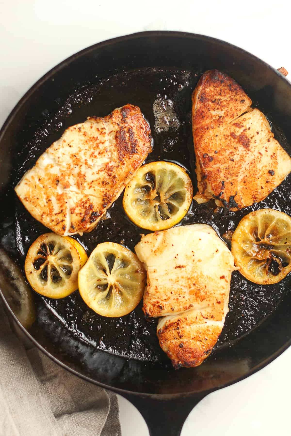 A cast iron skillet after pan searing the sea bass, with lemon slices.