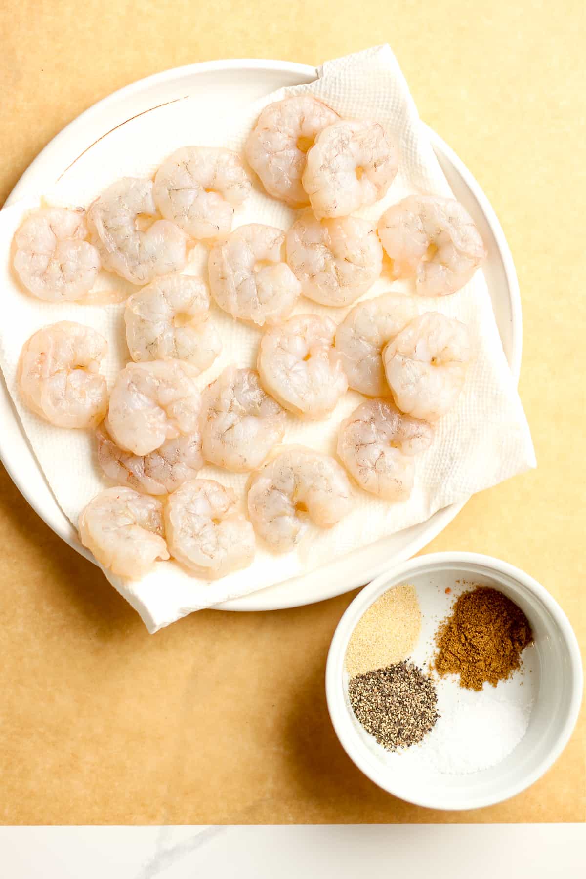 A plate of the raw shrimp, with a bowl of seasonings.