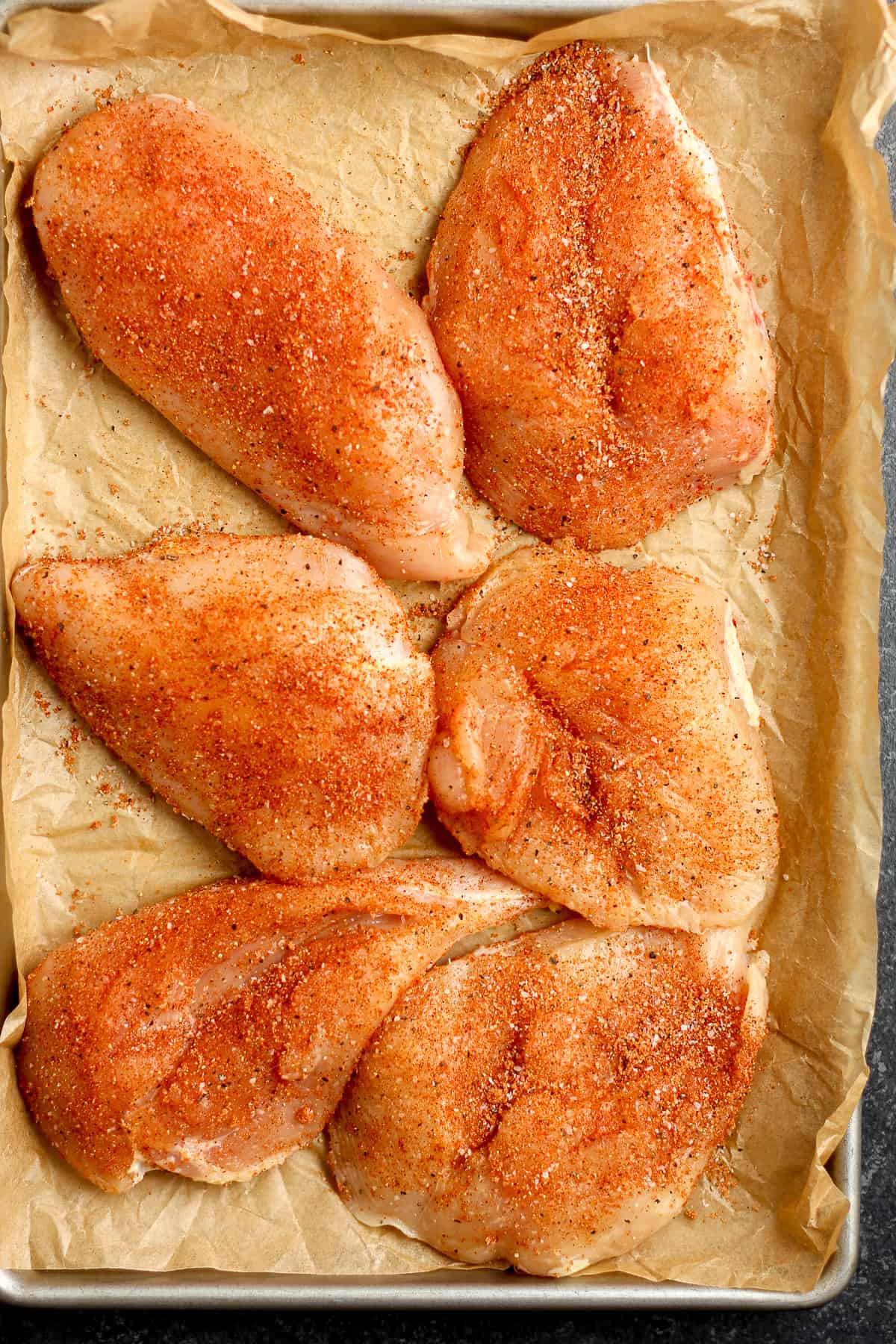 A pan of six raw and seasoned chicken breasts.