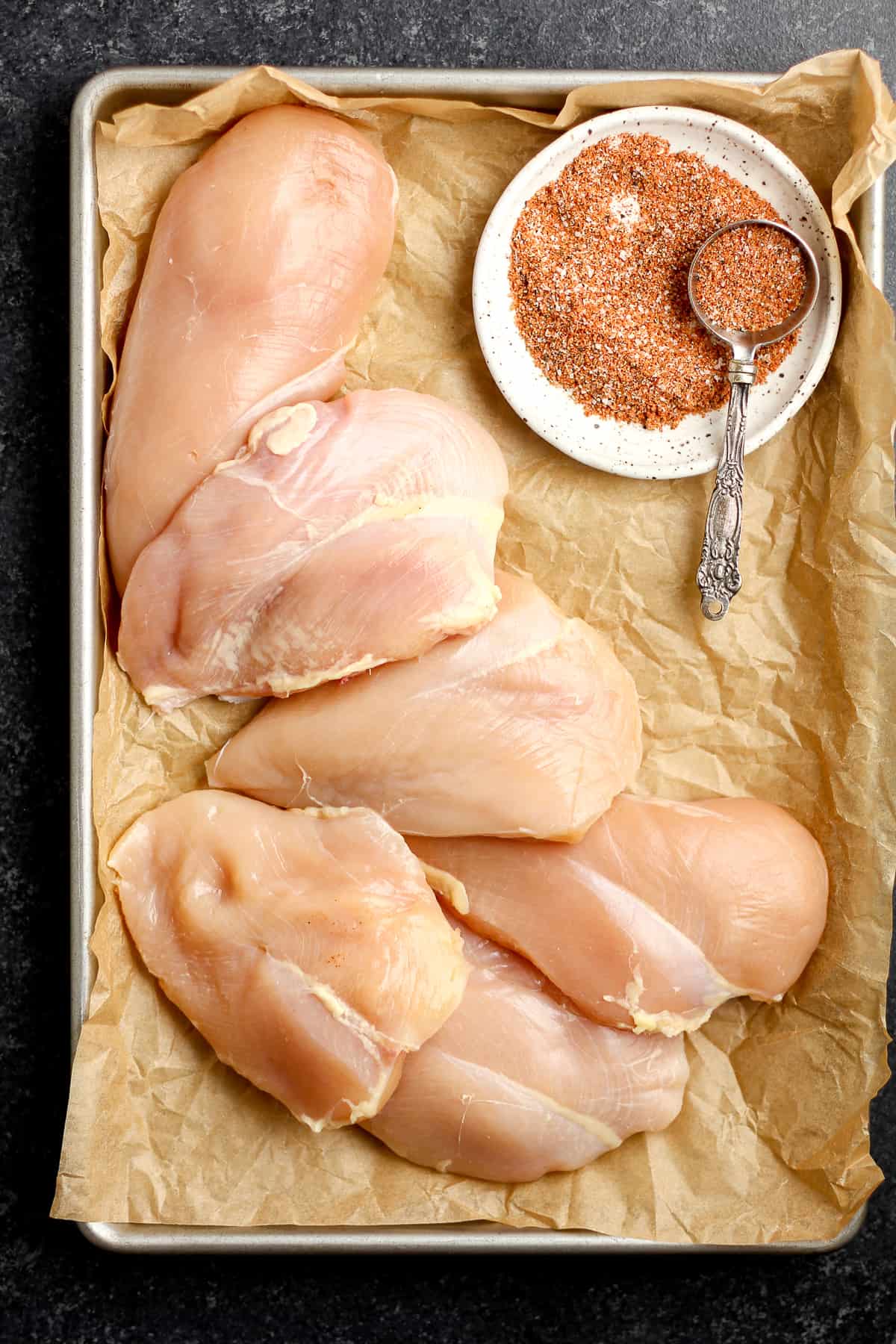 A pan of six raw chicken breasts with a plate of the best smoker rub.