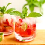Two glasses of strawberry mojitos with mint, lime, and fresh strawberries.