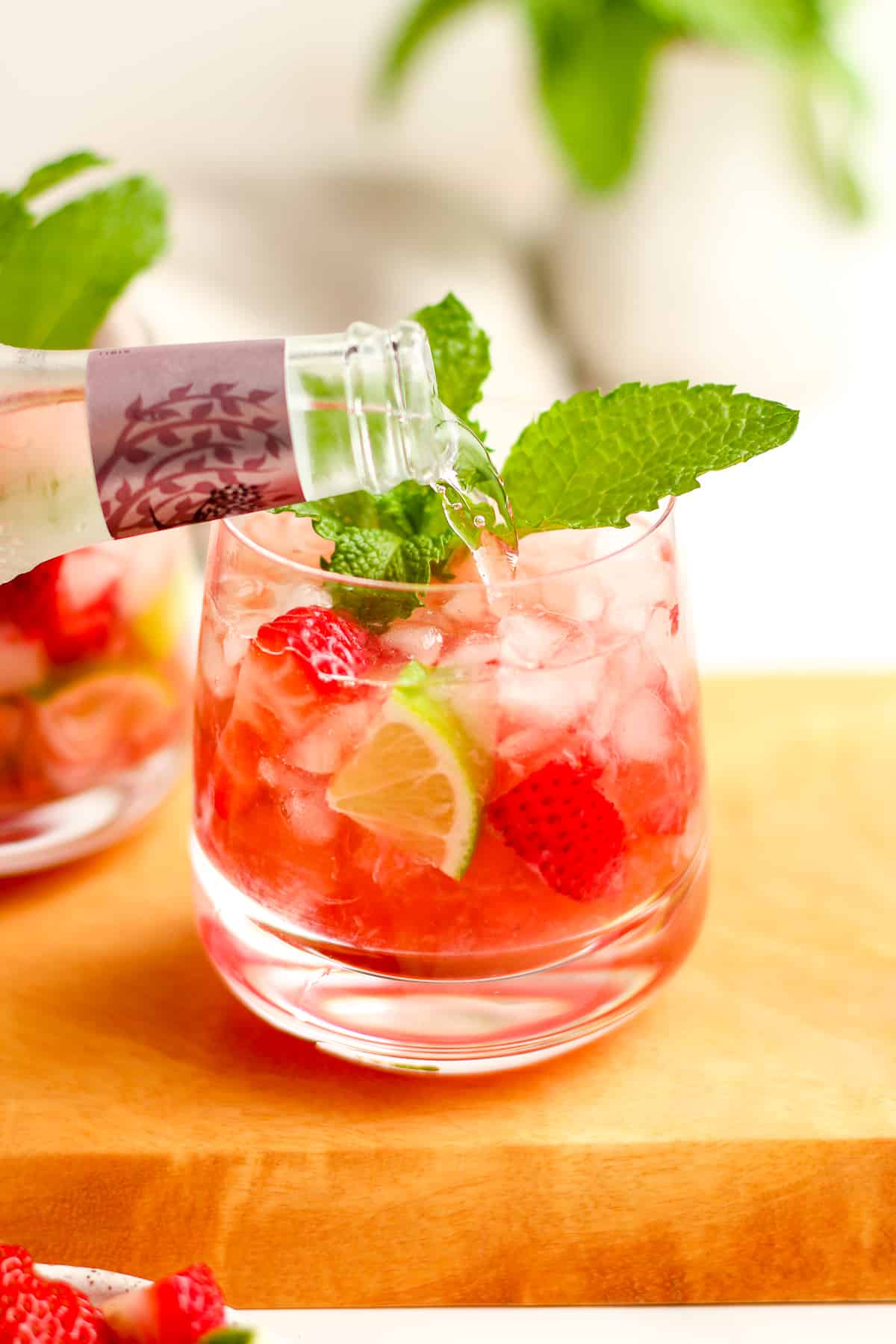 The club soda being added to the glass of strawberry mojitos.