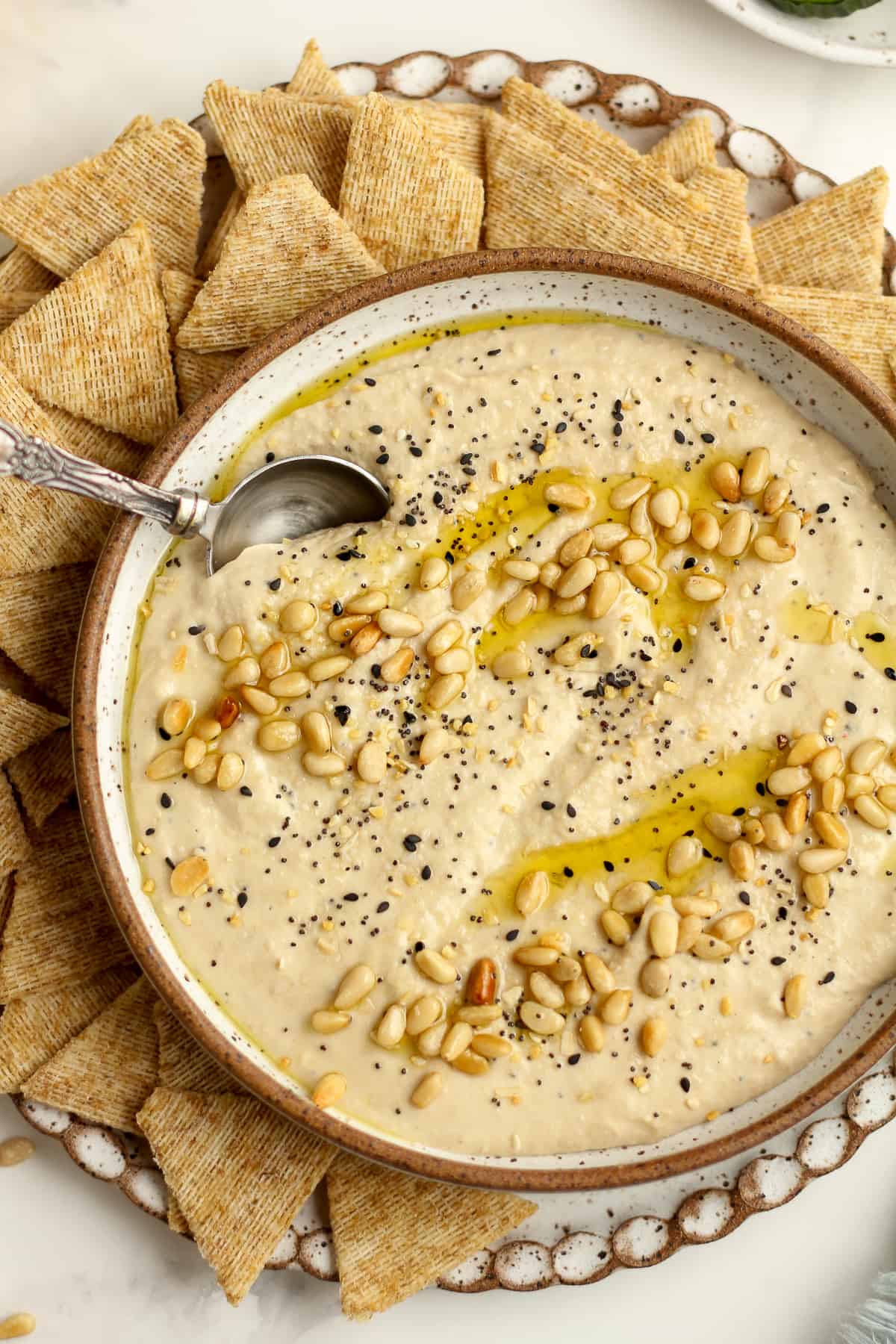 Closeup of a bowl of creamy toasted pine nut hummus with a spoon inside.
