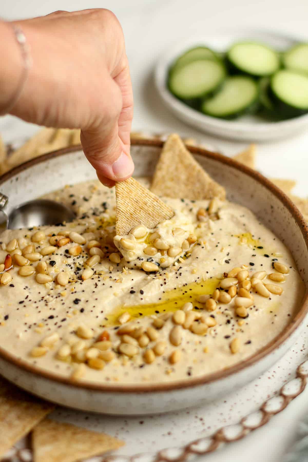 Side shot of my hand dipping a cracker in a toasted pine nut hummus bowl.