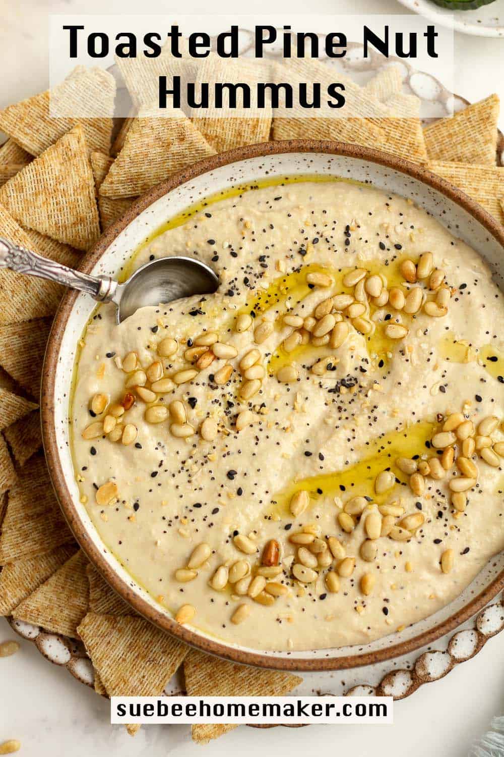 A bowl of toasted pine nut hummus with pine nuts on top, with crackers.