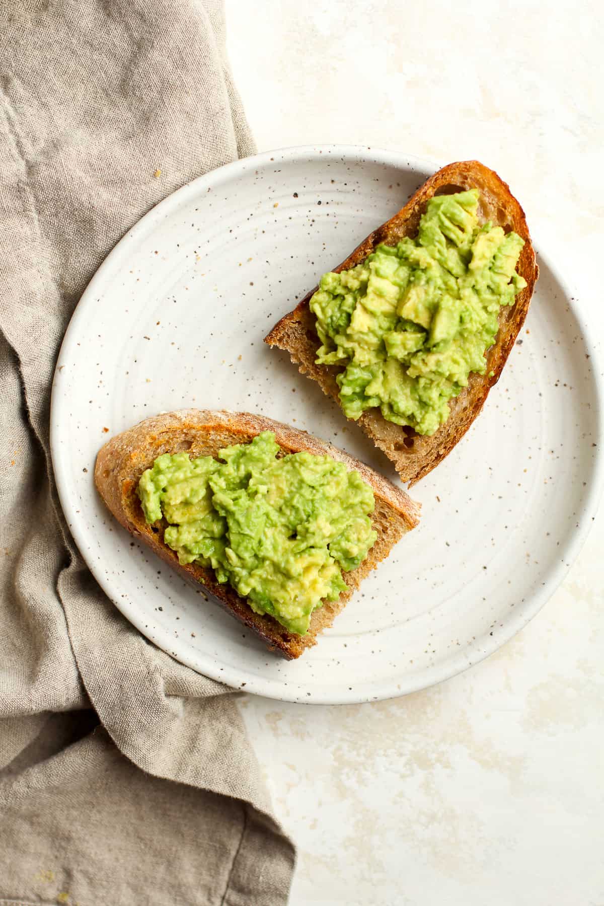 A plate with two halves multigrain toast with smashed avocado.