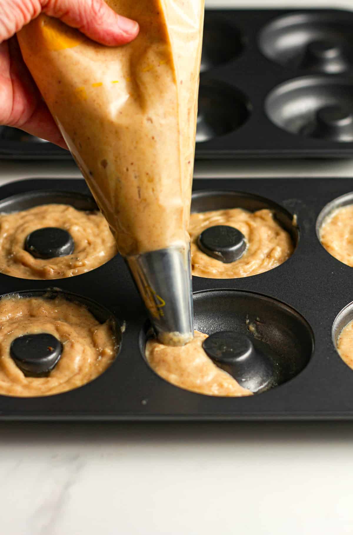Side view of a hand squeezing batter into a donut pan.