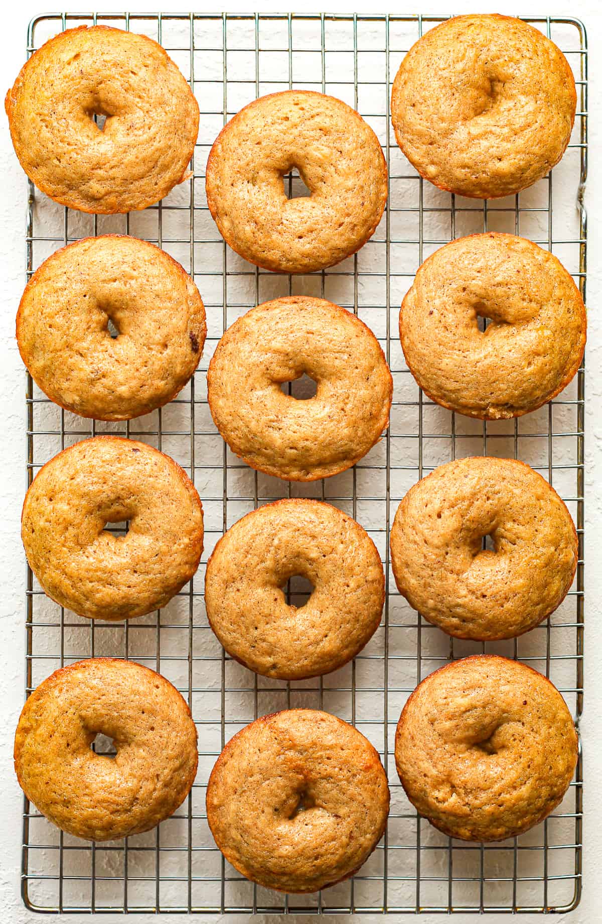 A cooling rack of 12 banana donuts.