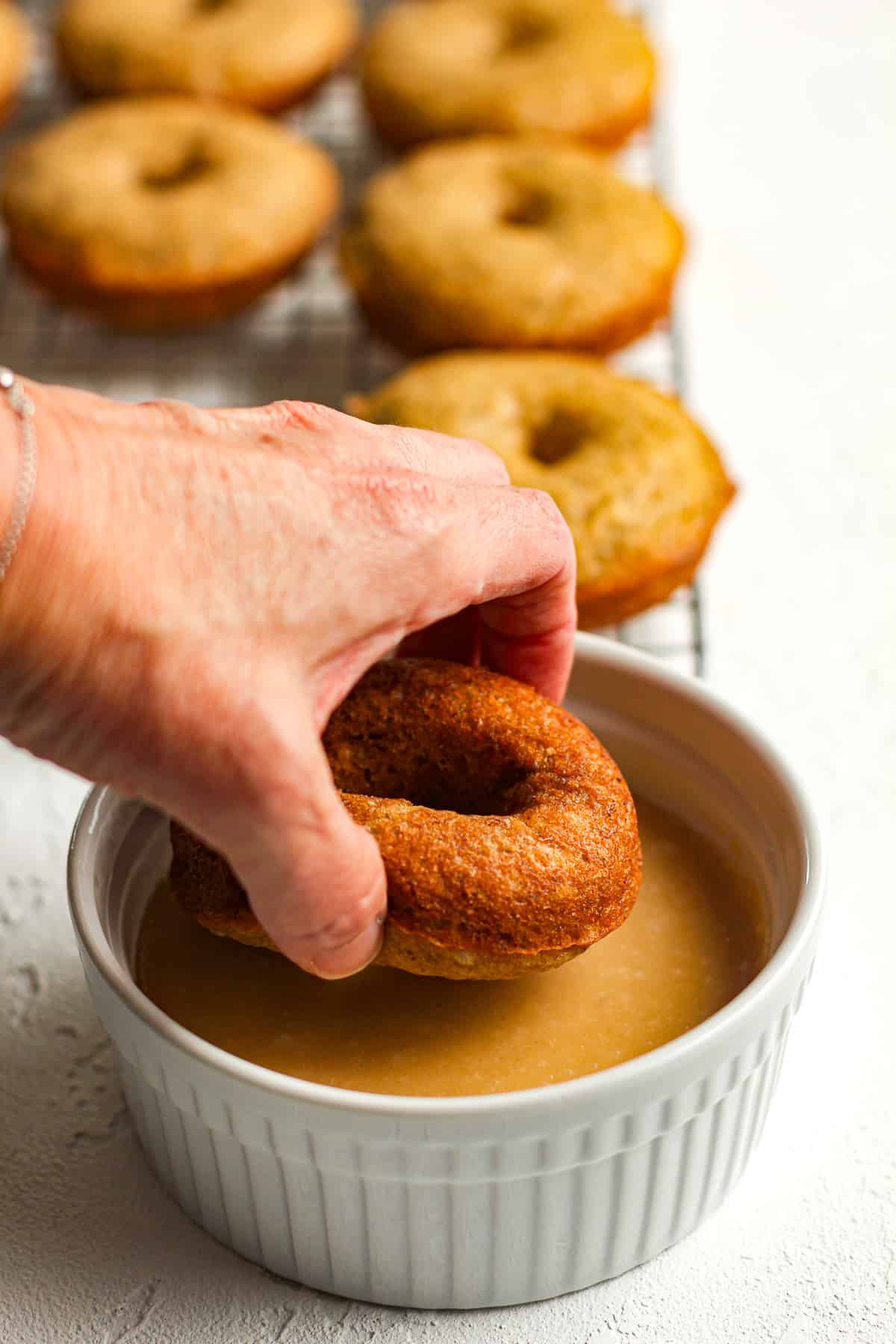 A hand dipping a donut in some brown sugar glaze.