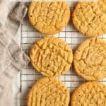 Eight peanut butter cookies on a cooling rack with a gray napkin.
