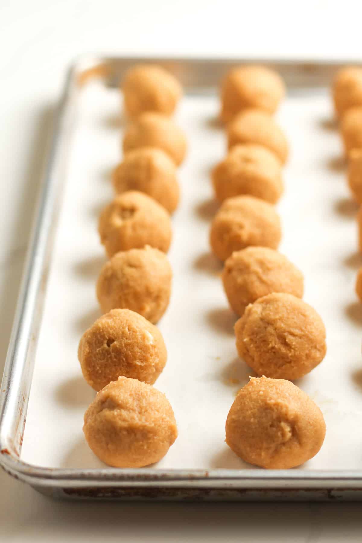 Side view of a pan of round balls of peanut butter cookie dough.