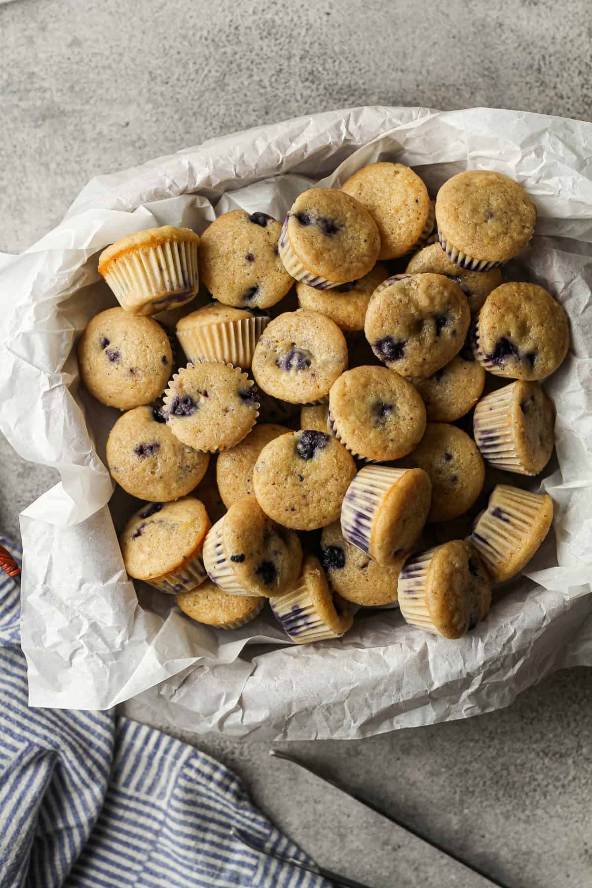 A basket of mini blueberry muffins, on a gray background.