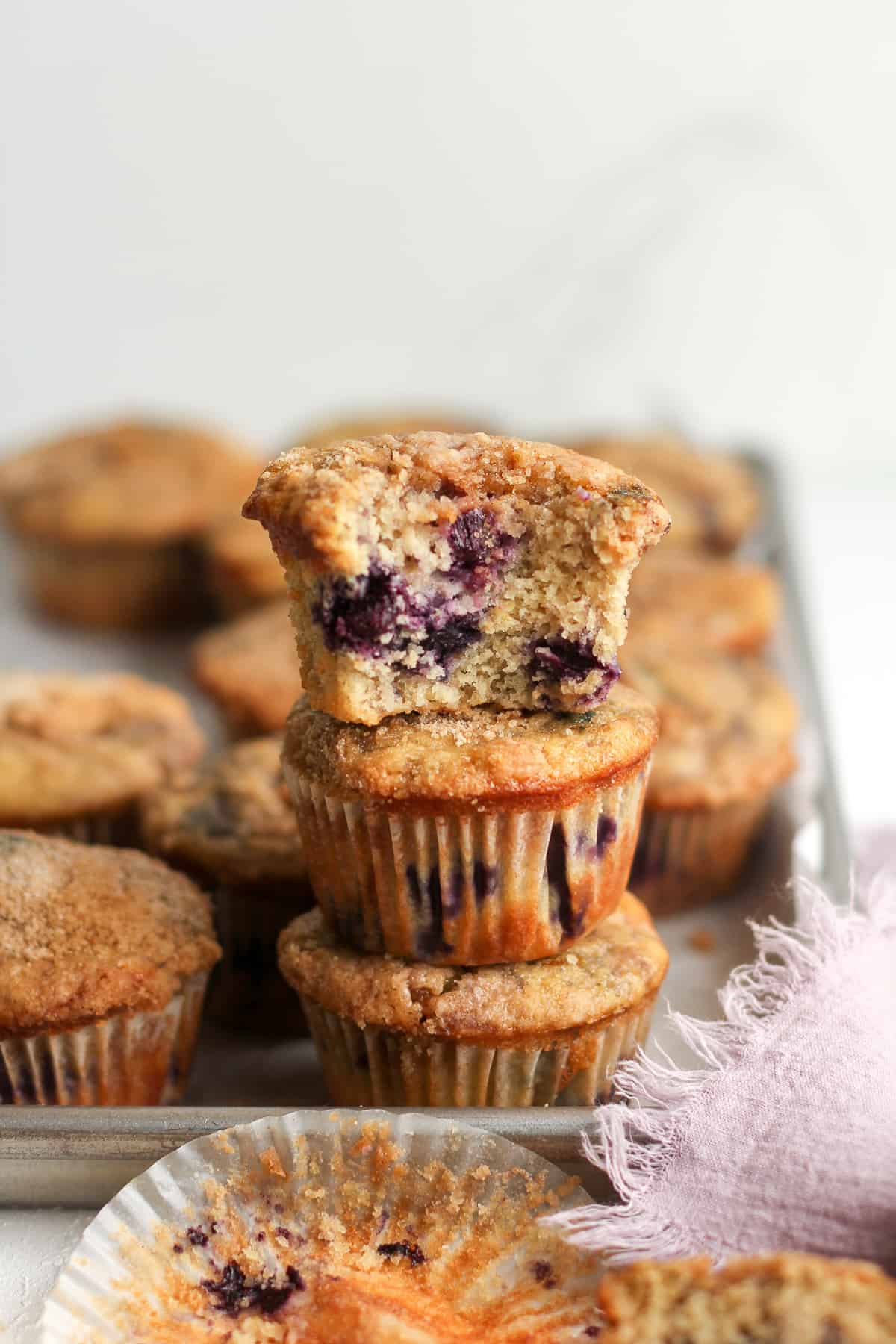 A stack of three blueberry streusel muffins on a tray of muffins.