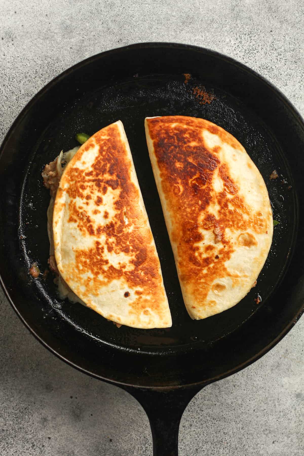 A skillet of two browned quesadillas.