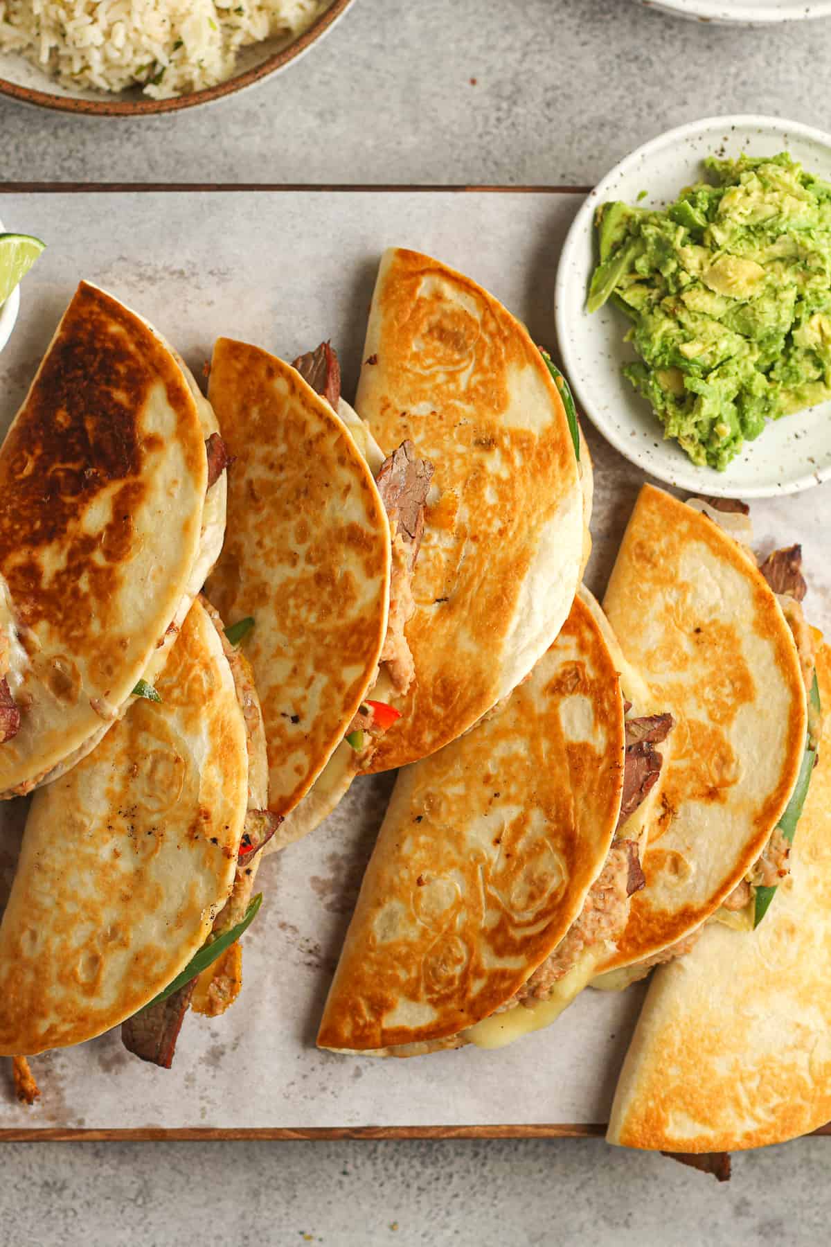 A board of just made carne asada quesadillas, with a plate of guacamole.