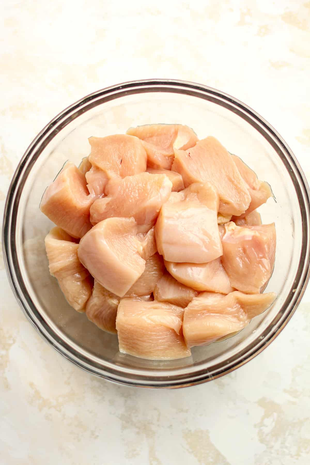 Raw chicken cubes in a glass bowl.
