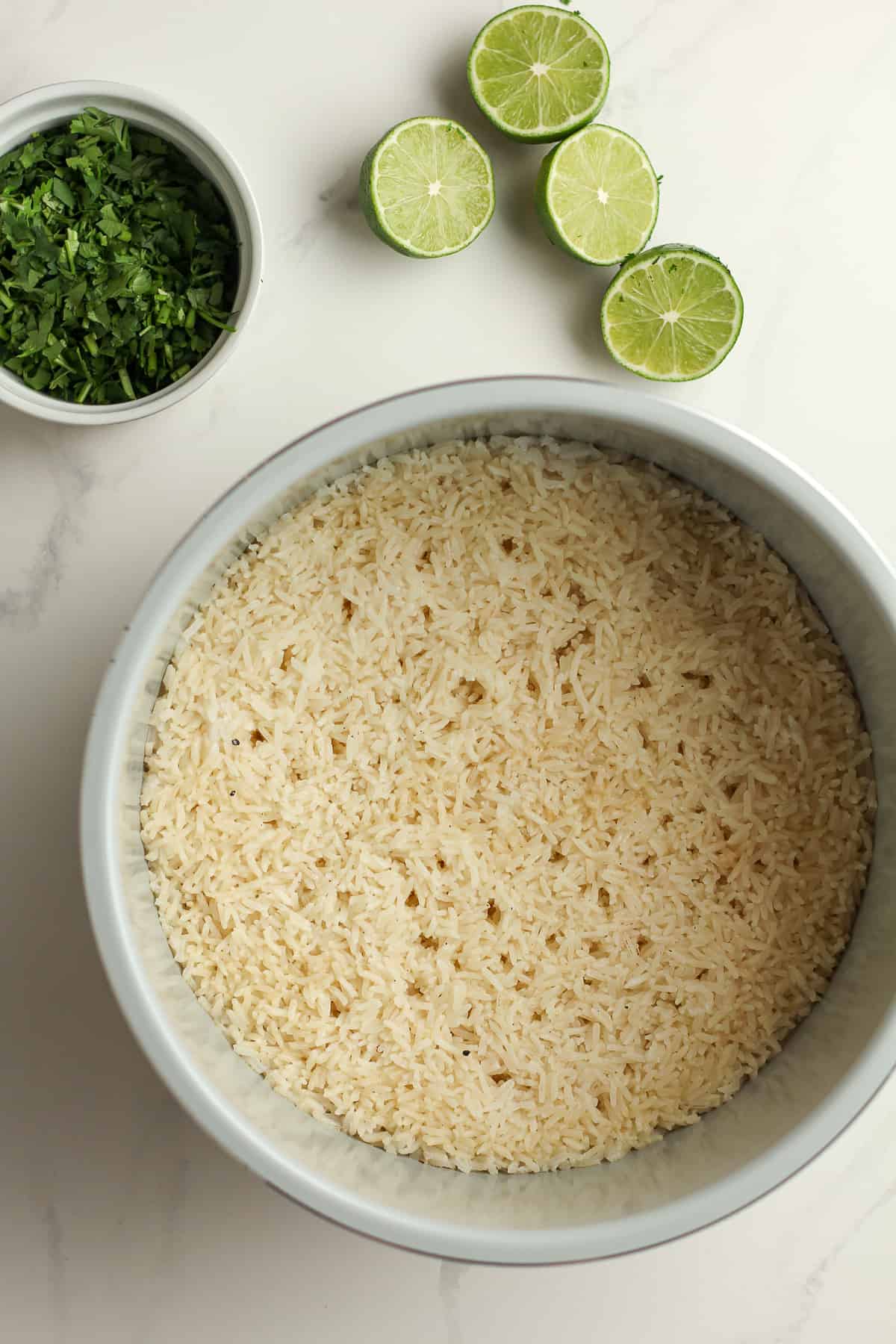 An instant pot of white rice with a bowl of cilantro and halved limes beside the pot.
