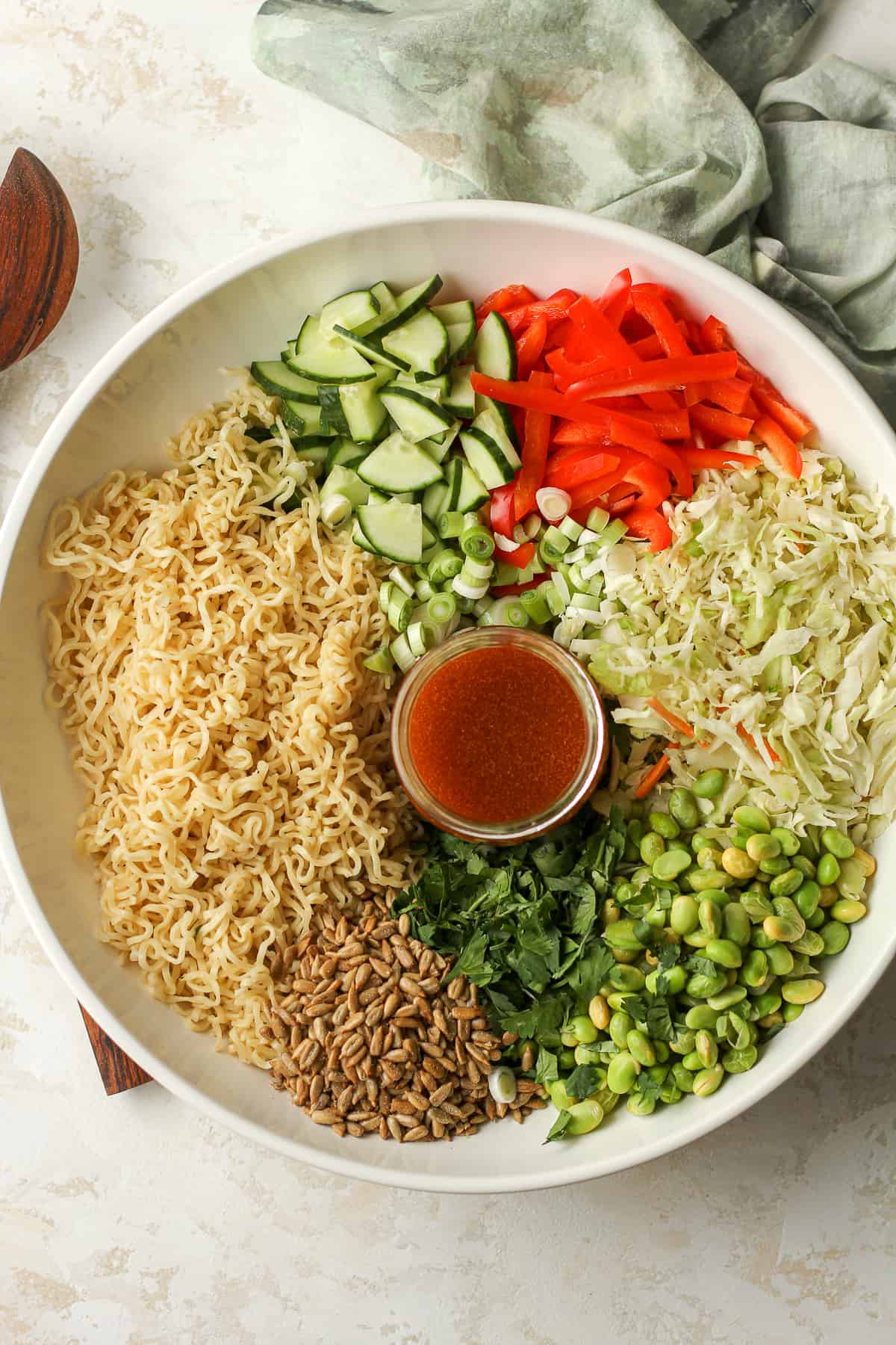 A bowl of the ramen salad with ingredients separated and a jar of dressing in the middle.